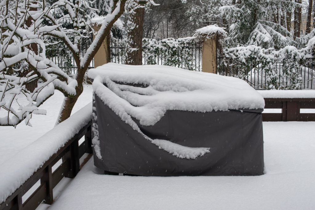 Snow covers covered furniture on a patio in winter.