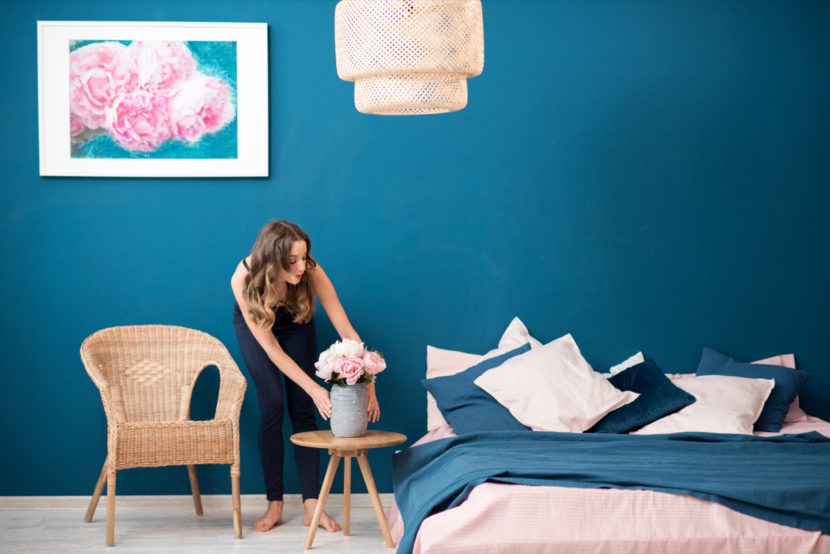 Young woman decorating bedroom with flowers at home.