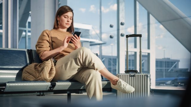 A woman sitting in the airport with her luggage while looking at her phone