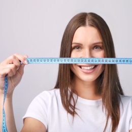 Beautiful young woman with measure tape on grey background