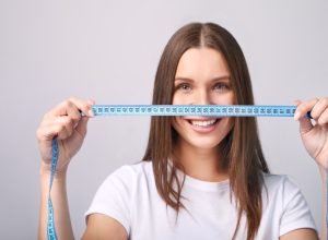 Beautiful young woman with measure tape on grey background