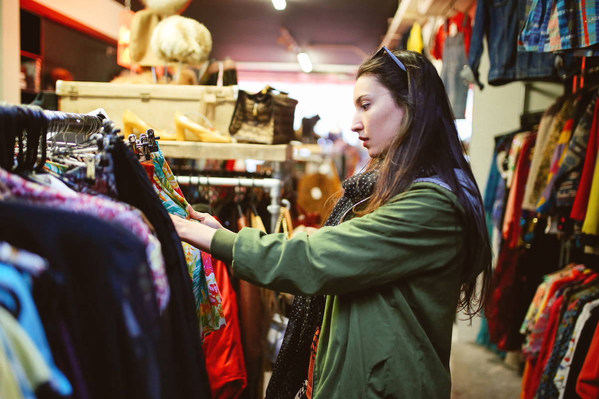 A woman looking through clothing racks at a thrift store.
