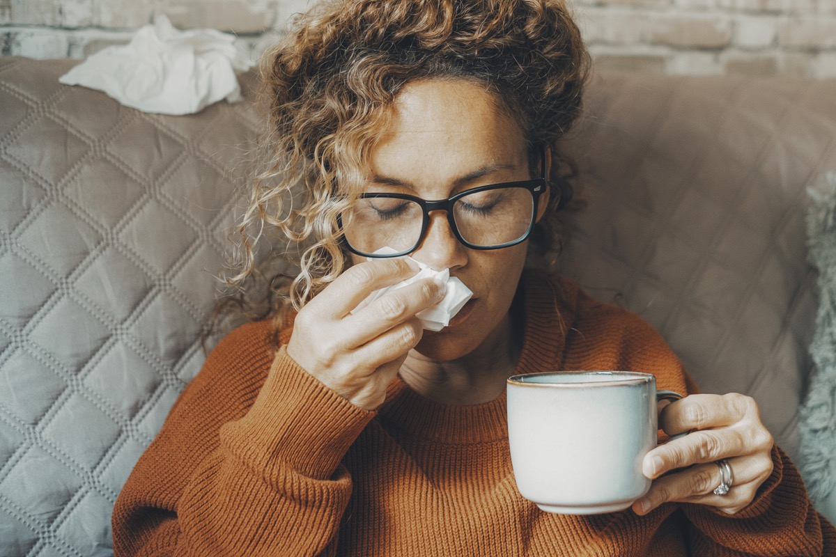 Sick woman at home blowing nose and take care of influenza virus disease. One female people using paper tissue and drink herbal tea medicine alone at home. Concept of flu cold in winter season indoor
