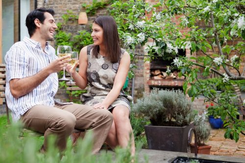 Woman flirting and touching man's knee while they drink wine together in a garden.