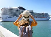 Tourist girl with backpack and hat standing in front of big cruise liner