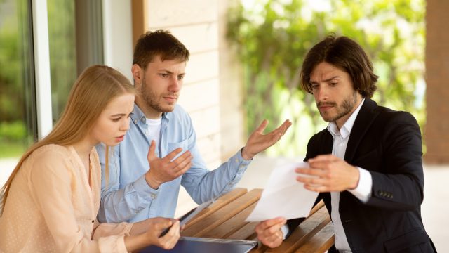 Millennial couple dissatisfied with real estate purchase agreement terms and realtor in front of house