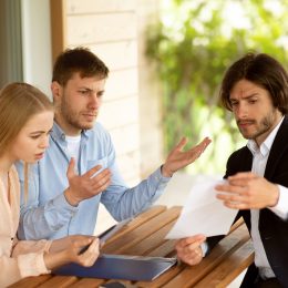 Millennial couple dissatisfied with real estate purchase agreement terms and realtor in front of house