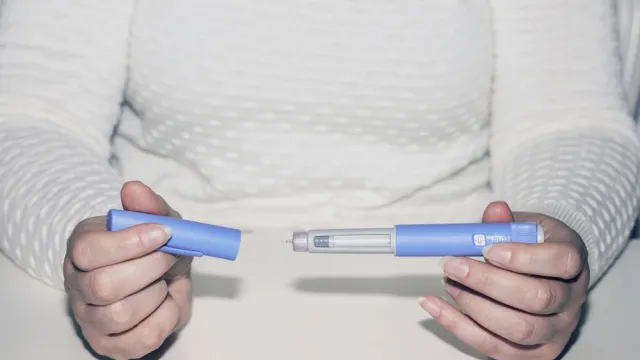 A close up of a person holding a diabetes or weight loss drug injection device