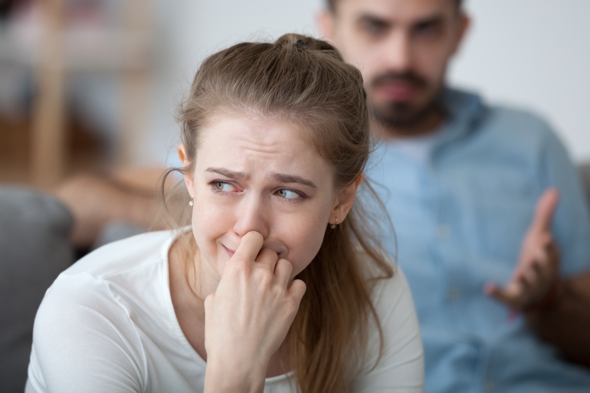 Woman in foreground crying while a man in the background looks angry at her