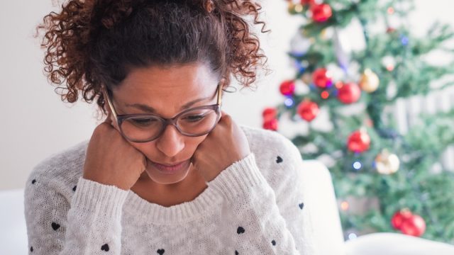 Worried black young woman sitting in the living room at home during christmas holiday