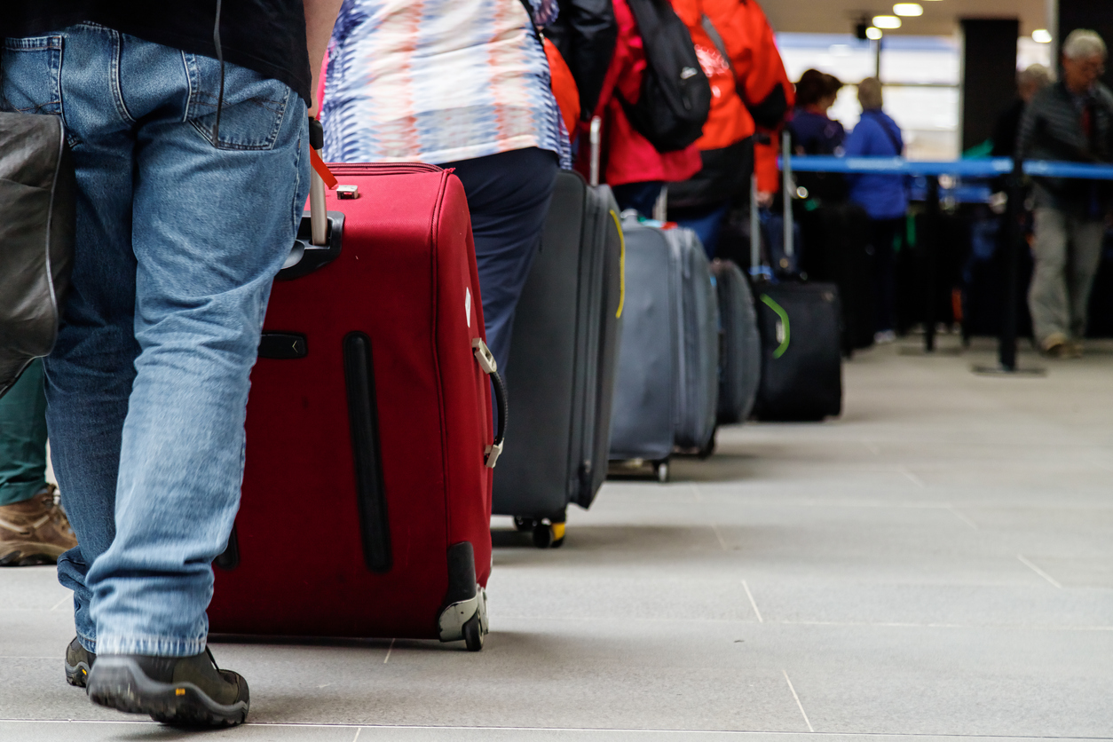 A close up of a group of travelers waiting in line with their bags for security or to check in