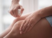 Woman is spraying a pain reliever on her knees close up.