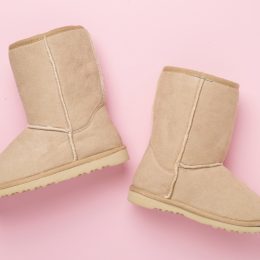A pair of beige Ugg boots on a pink background.