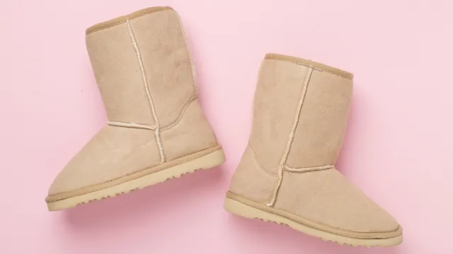 A pair of beige Ugg boots on a pink background.
