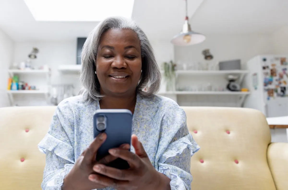Happy mature woman at home looking at social media on her cell phone - lifestyle concepts
