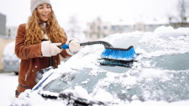 Young woman cleaning snow from car with brush. Transport, winter,  people and vehicle concept.