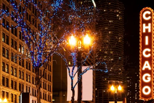 Photo of Chicago's Illuminated sign, at night. Buildings and trees with christmas ornaments.