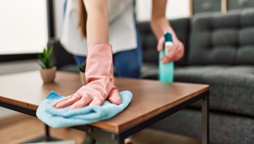 Close up of a woman wearing pink gloves cleaning her coffee table with a blue rag