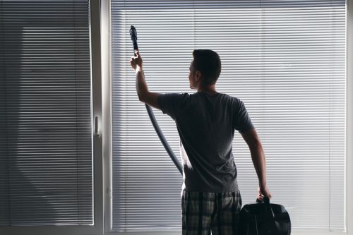 Man cleaning dust from window blind with a vacuum cleaner