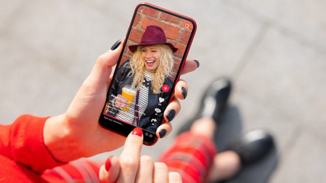 Close up of a woman with red fingernails watching a TikTok video on her phone