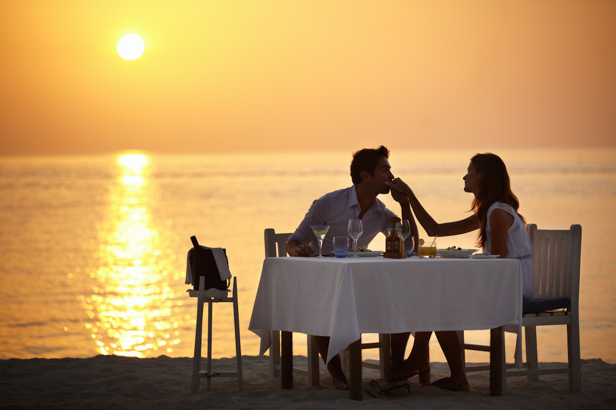 A young man kissing the hand of his wife while having dinner on the beach