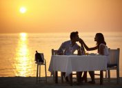 A young man kissing the hand of his wife while having dinner on the beach