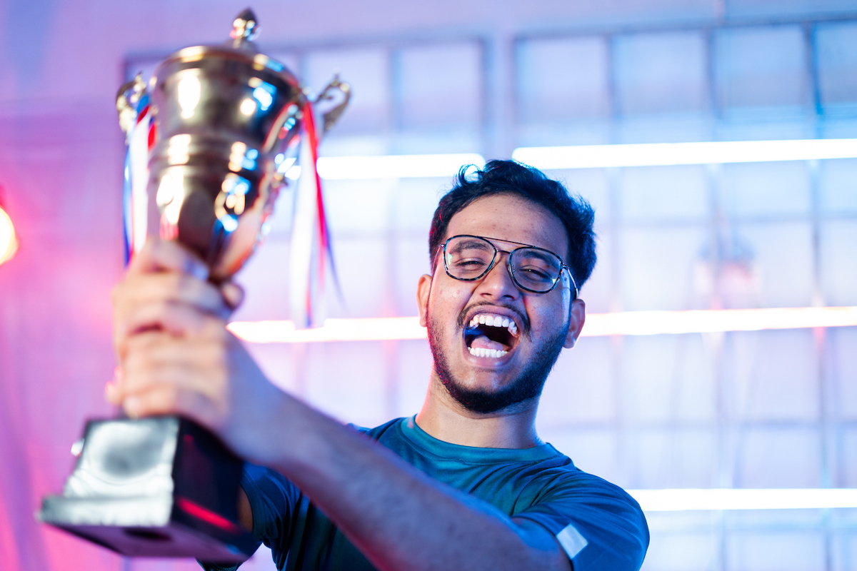 An excited man celebrating a victory, holding up a big silver trophy.