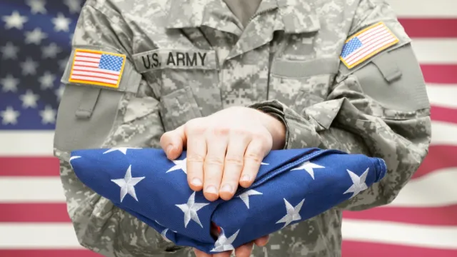 U.S. Army young soldier holding carefully folded USA flag in front of his chest