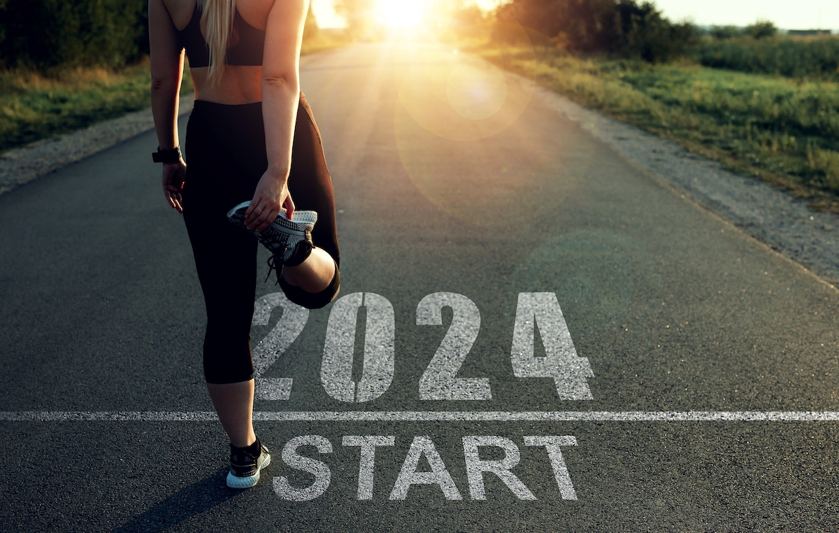 A female runner stretching before starting down a road marked "2024."