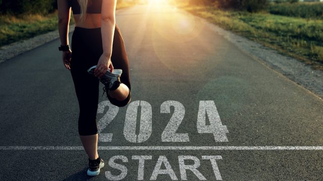 A female runner stretching before starting down a road marked "2024."