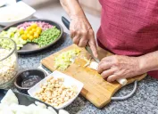 Hands of an elderly woman cutting onions with several legumes.