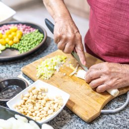 Hands of an elderly woman cutting onions with several legumes.