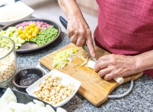 Hands of an elderly woman cutting onions with several legumes.