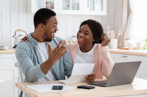 A happy couple with excited looks on their faces holding a letter in front of their computer, potentially getting a tax refund