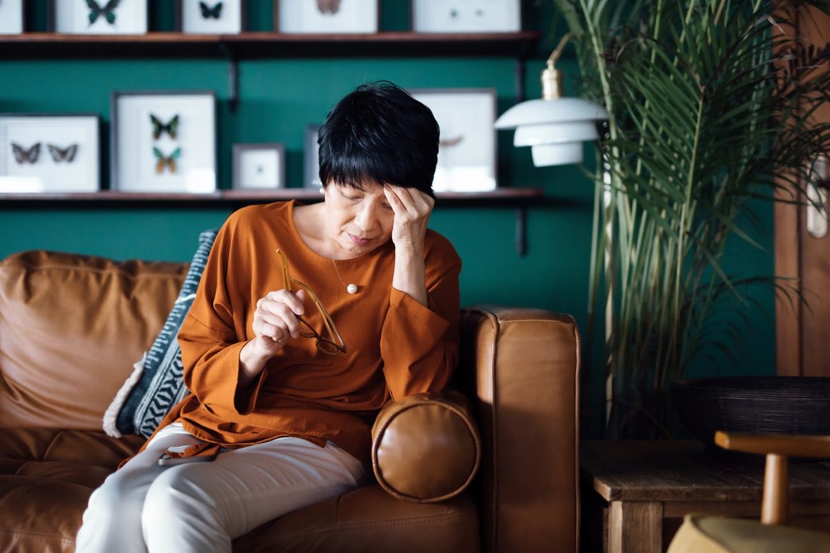 woman feeling fatigued while sitting on her couch, resting her head in her hand