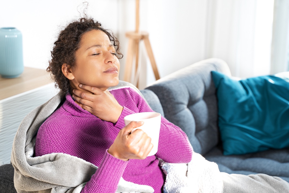 woman with a sore throat sitting on the couch holding a cup of tea