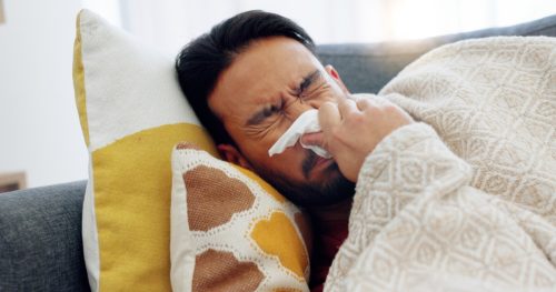 congested man lying on couch blowing nose