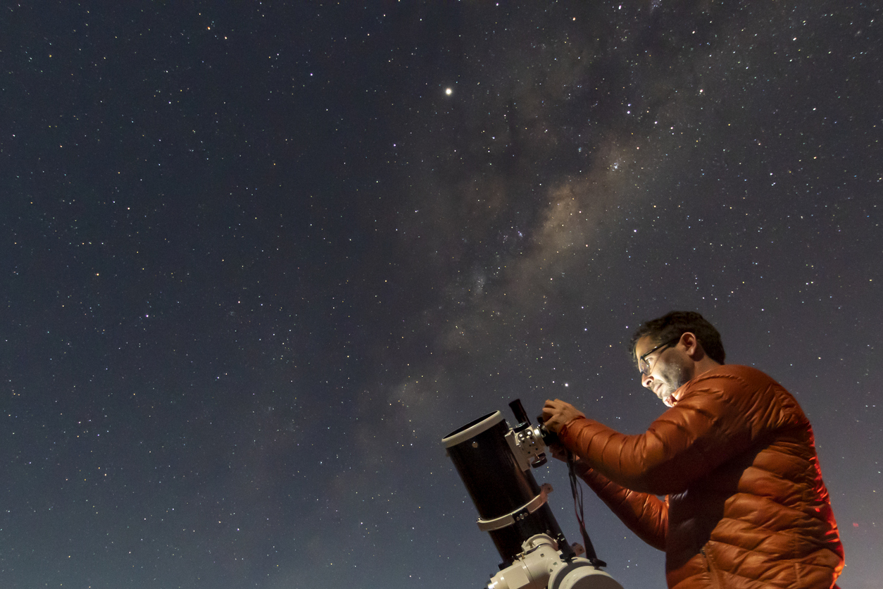 A person setting up a telescope to look at the night sky filled with stars