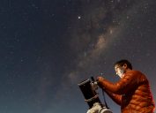 A person setting up a telescope to look at the night sky filled with stars