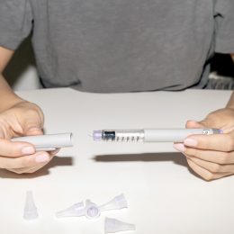 A close up of a person taking the cap off a weight loss drug injection needle