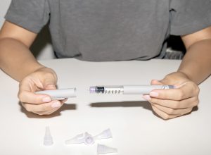 A close up of a person taking the cap off a weight loss drug injection needle