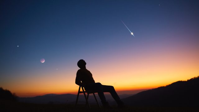 A person sitting in a chair while stargazing as a meteor travels overhead
