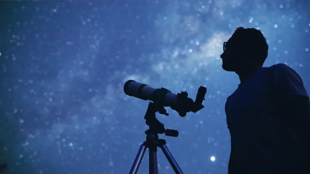 The silhouette of a person looking at the night sky and Milky Way with a telescope