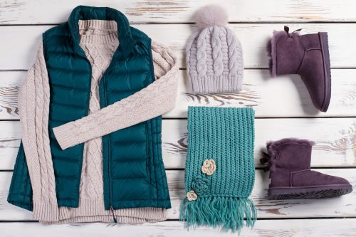 Winter sweater and vest, along with accessories and boots in teal and purple colors on a wooden background
