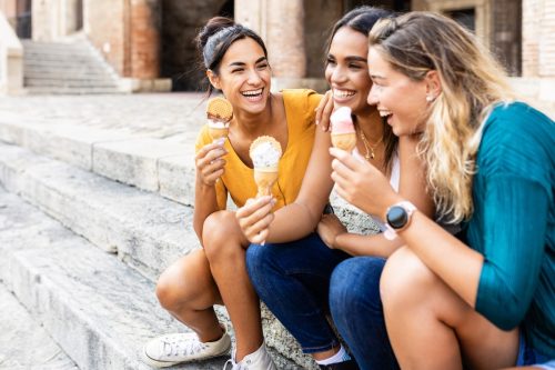 group of women eating ice cream on the curb and laughing
