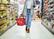 Supermarket, grocery and phone with a black woman shopping for a sale or discount in a convenience store. Legs, walking and food with a female customer in the groceries product aisle of a shop
