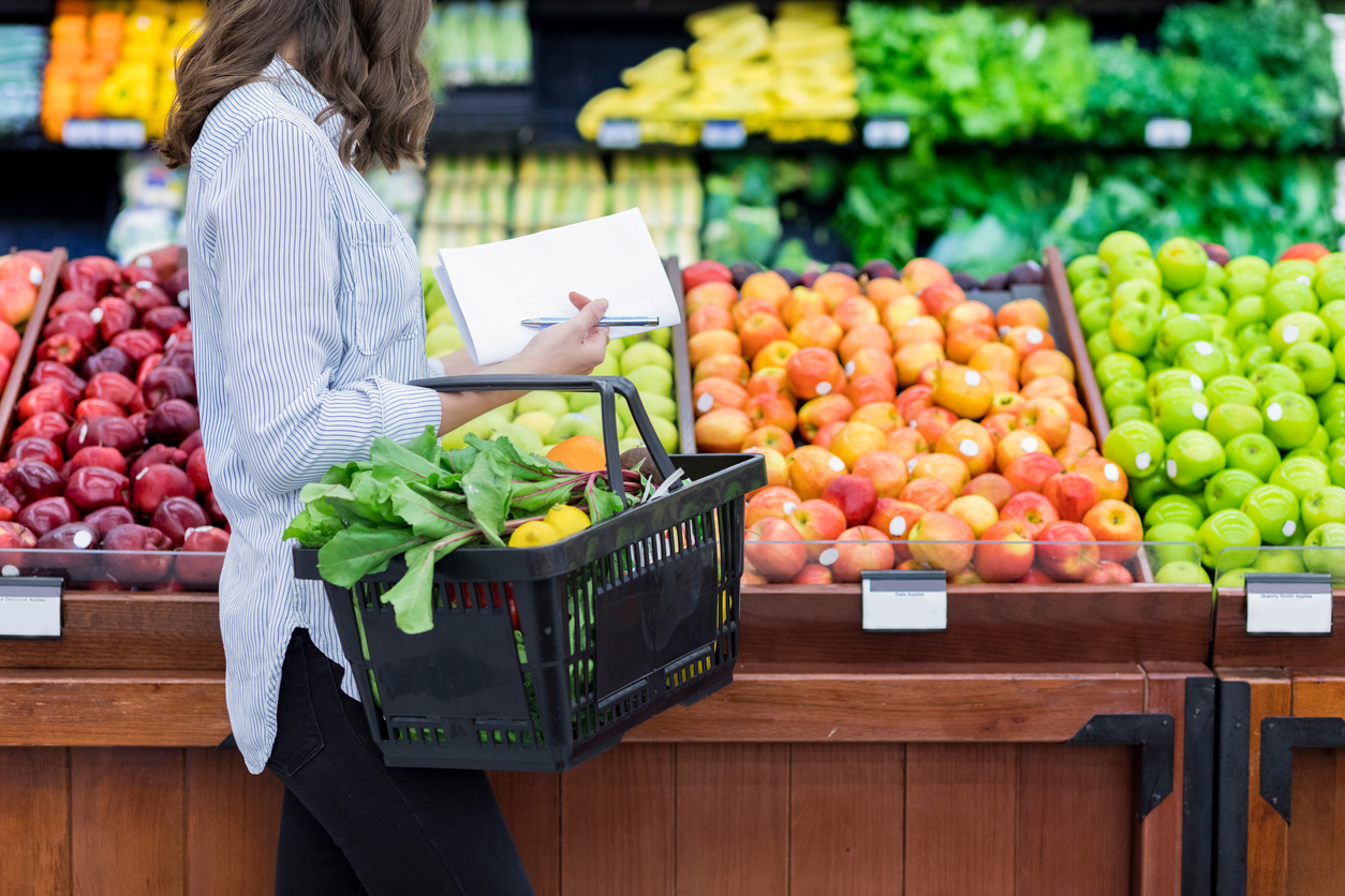 A woman shopping for produce using a hand basket in the grocery store