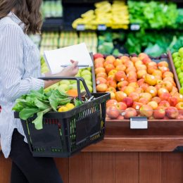 A woman shopping for produce using a hand basket in the grocery store
