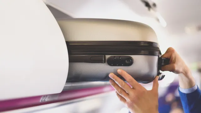 Traveler putting carry-on suitcase in overhead bin on airplane
