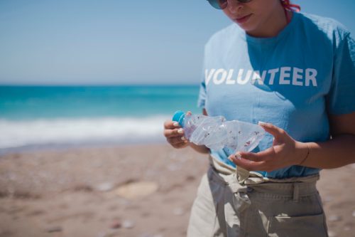 A woman in a blue T-shirt collects garbage on the beach.